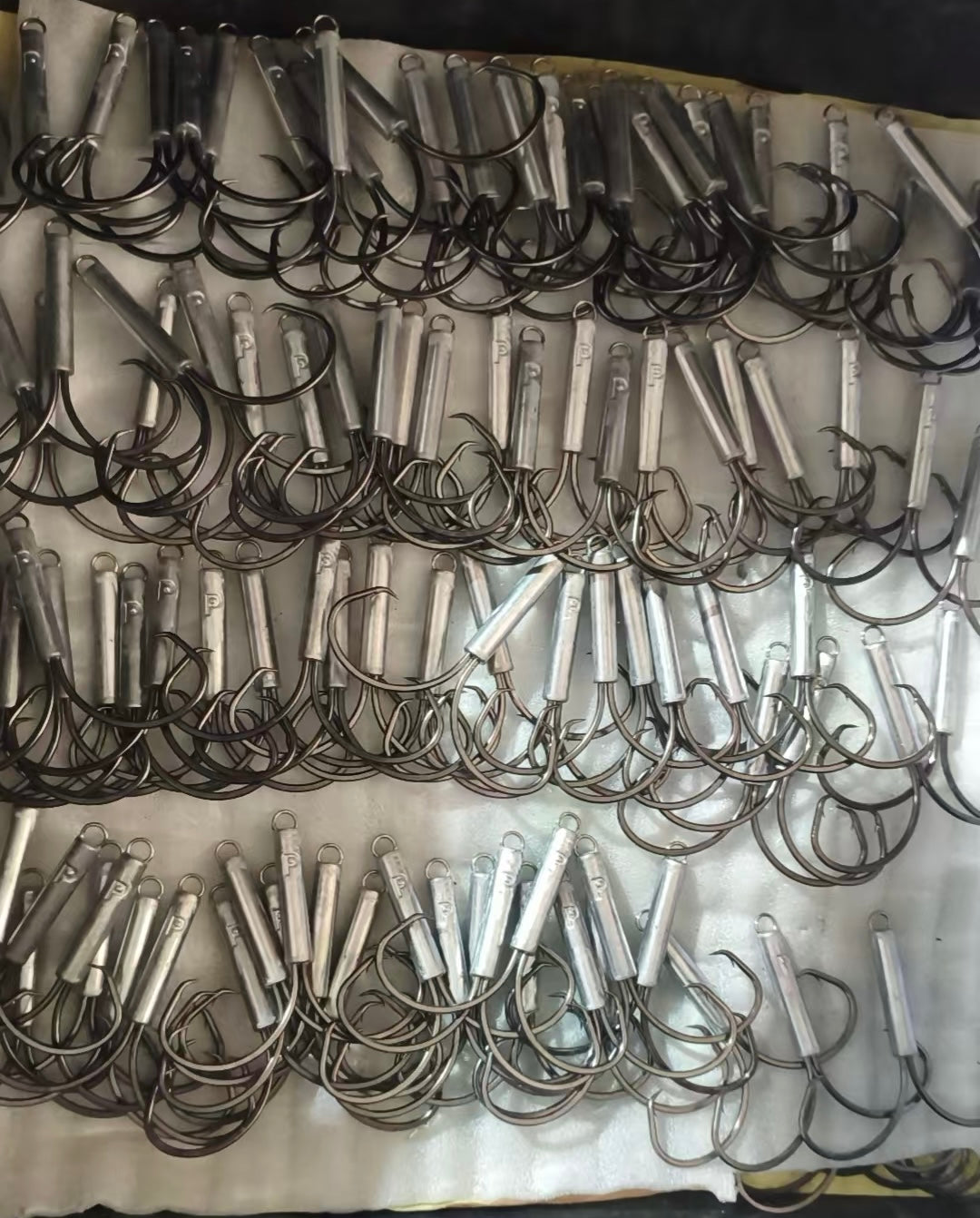 Rows of silver cylindrical jig heads with dark circle hooks on gray fabric